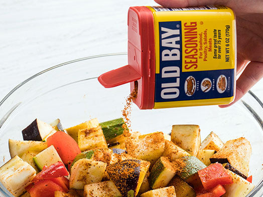 pouring old bay seasoning into a bowl of cut vegetable